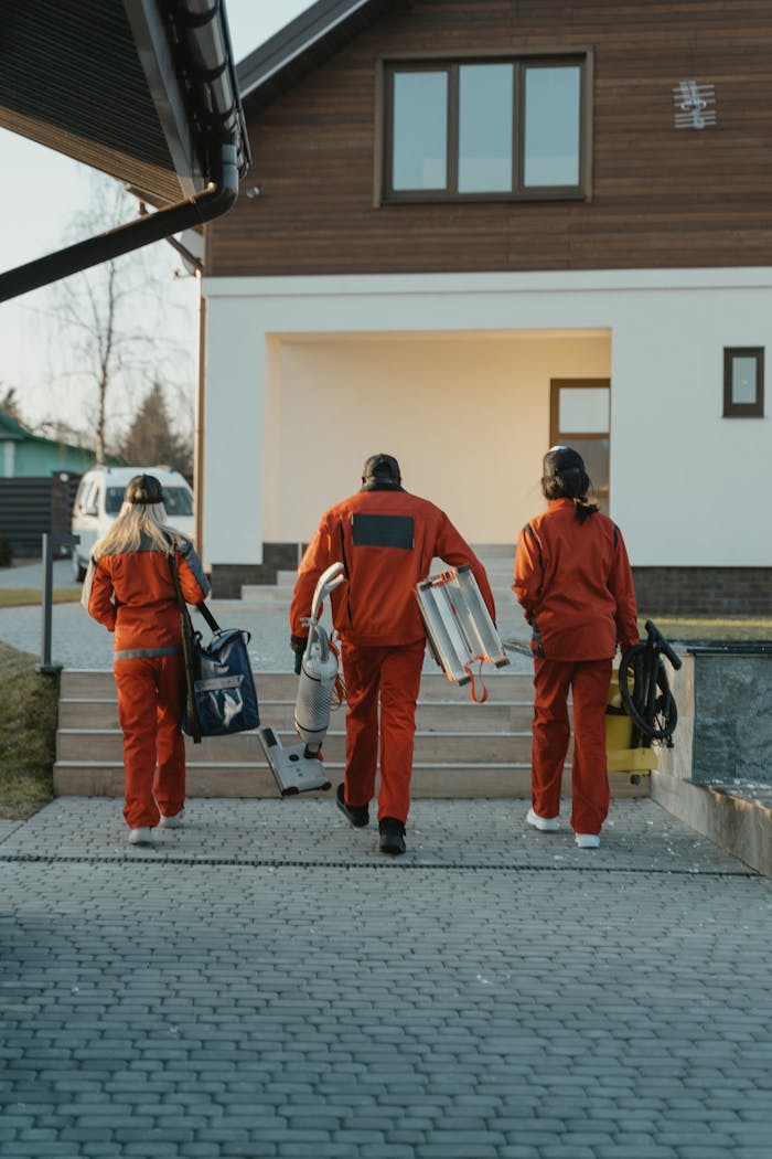 services-02 Cleaning crew in red uniforms with equipment approaching a modern house exterior.