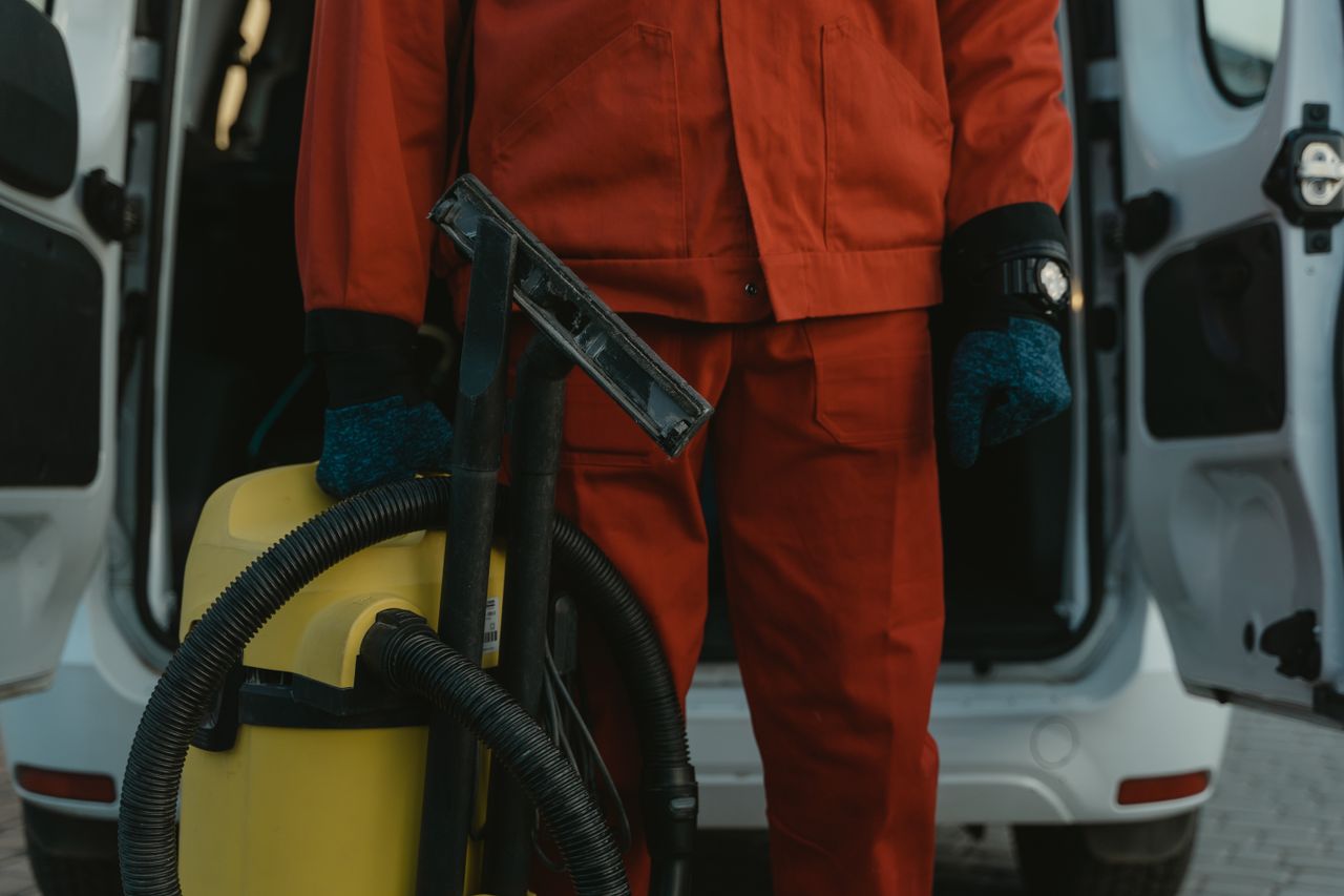 hero-img-01 A professional cleaner in a red uniform holding a vacuum near a van, ready for service.